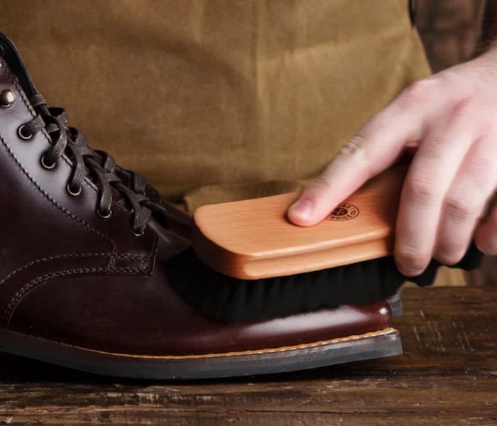 a cobber using a horsehair brush to clean a smooth leather boot