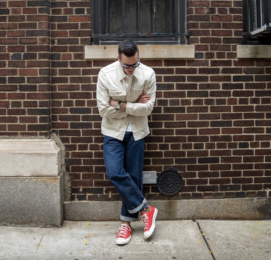 Nick in the white chore coat, blue jeans, and converse shoes on the street